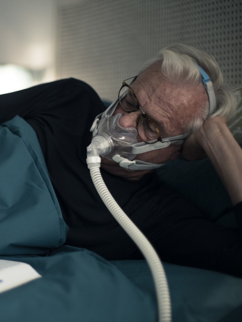Starszy mężczyzna leży w łóżku, używając maski tlenowej do oddychania.