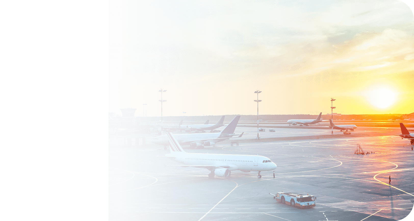 Samoloty stoją na płycie lotniska o wschodzie słońca, widoczne pasy startowe i pojazdy lotniskowe.