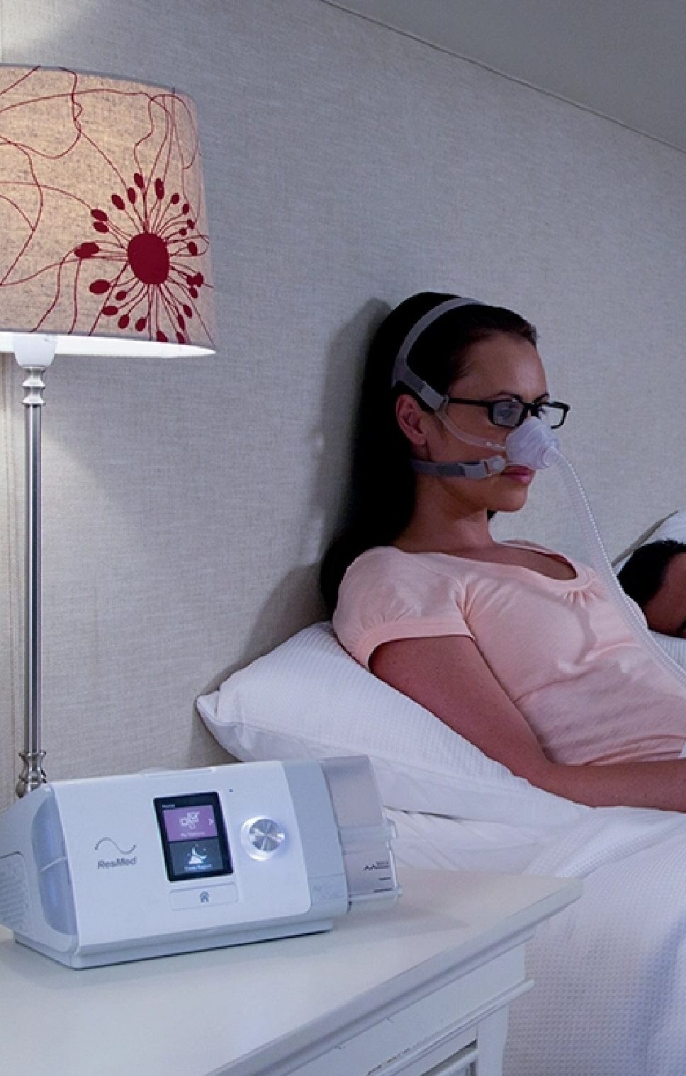 Kobieta leży w łóżku, nosi maskę tlenową podłączoną do aparatu medycznego CPAP.