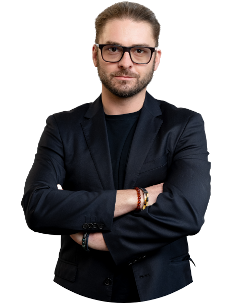 Mężczyzna w okularach i garniturze stoi z założonymi rękoma i patrzy przed siebie.