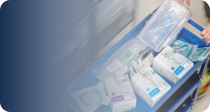 Wózek medyczny z respiratorami i akcesoriami, widoczne dłonie osoby przygotowującej sprzęt.