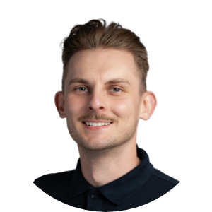 Mężczyzna w ciemnej koszuli uśmiecha się do aparatu na białym tle.