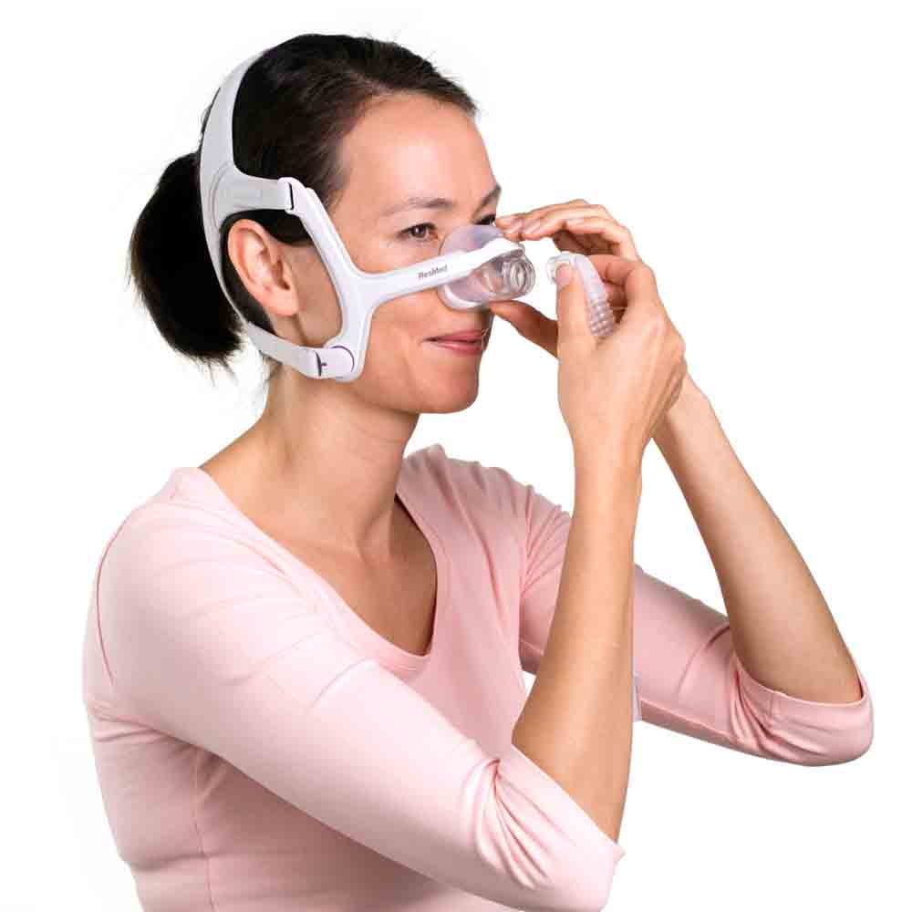 maska-nosowa-dla-kobiet-cpap-airfit-n20-for-her-resmed Kobieta zakłada maskę CPAP na nos do terapii bezdechu sennego.