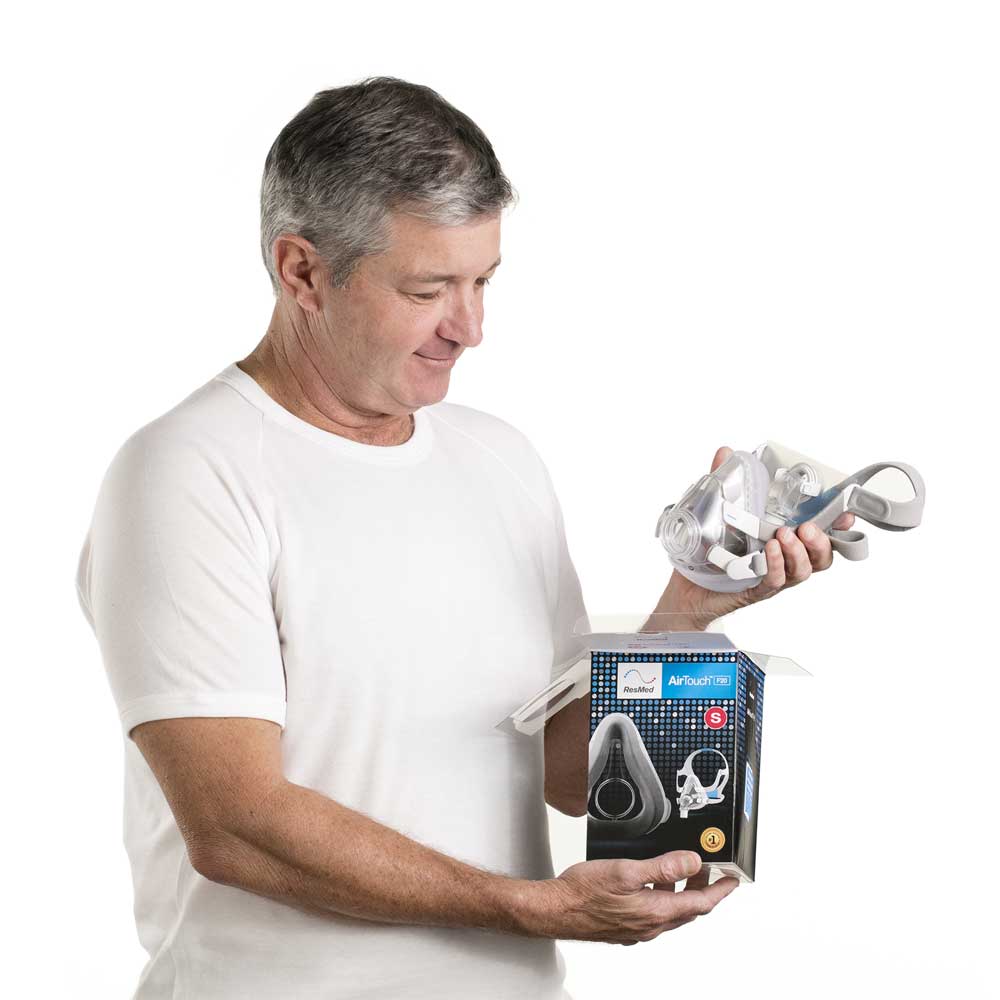 p-EU-63034-ResMed-AirTouch-comfortable-CPAP-mask-02-Medium Mężczyzna wyjmuje maskę CPAP z pudełka i ogląda ją z zainteresowaniem.